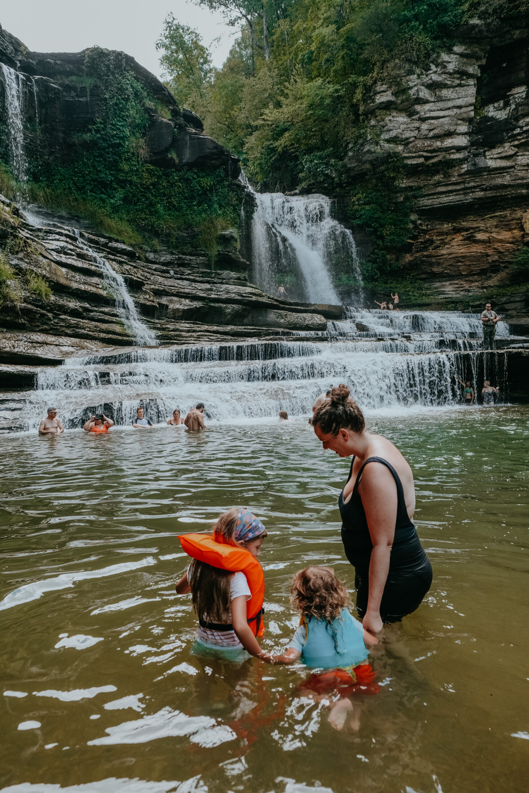 Woman with two young children swimming at the base of a waterfall at Cummins Fall State Park